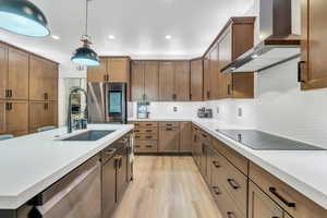 Kitchen featuring wall chimney exhaust hood, hanging light fixtures, stainless steel appliances, light countertops, and a sink