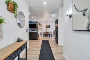 Hallway featuring baseboards, light wood finished floors, a notable chandelier, and recessed lighting