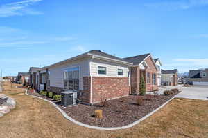 View of side of home with a yard, central AC unit, a residential view, and brick siding