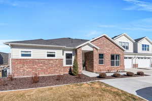 View of front of home with brick siding, an attached garage, board and batten siding, central AC, and driveway