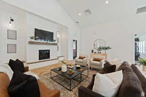 Living area featuring visible vents, baseboards, high vaulted ceiling, and a glass covered fireplace