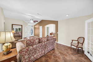 Living area featuring baseboards, arched walkways, vaulted ceiling, and a ceiling fan