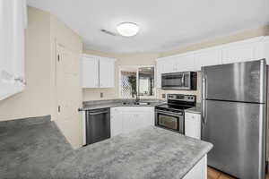 Kitchen with stainless steel appliances, a peninsula, a sink, visible vents, and white cabinetry