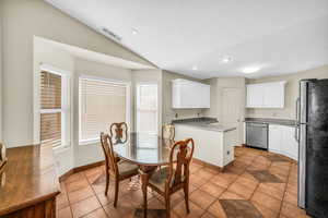 Dining room featuring light tile patterned floors, visible vents, vaulted ceiling, a textured ceiling, and baseboards