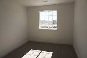 Empty room featuring visible vents, dark carpet, and baseboards