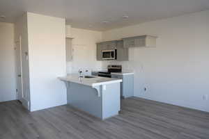 Kitchen with appliances with stainless steel finishes, a breakfast bar, wood finished floors, a peninsula, and a sink