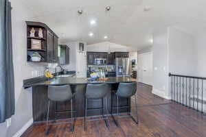 Kitchen with dark wood finished floors, dark countertops, stainless steel appliances, open shelves, and a sink