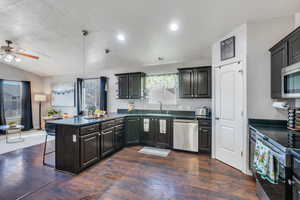 Kitchen featuring dark countertops, a peninsula, appliances with stainless steel finishes, and a breakfast bar area