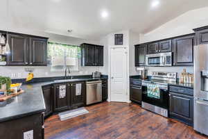 Kitchen with lofted ceiling, stainless steel appliances, a sink, dark countertops, and dark wood finished floors