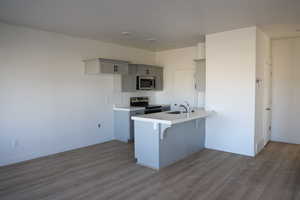 Kitchen with a breakfast bar area, stainless steel appliances, a peninsula, a sink, and gray cabinets