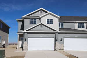 View of front facade featuring board and batten siding, concrete driveway, stone siding, and a garage