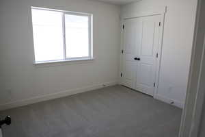 Unfurnished bedroom with light carpet and baseboards