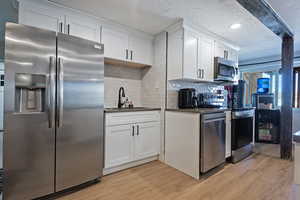 Kitchen featuring stainless steel appliances, light wood finished floors, dark countertops, and a sink