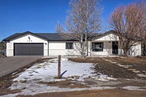 Ranch-style home with an attached garage, aphalt driveway, metal roof, and brick siding