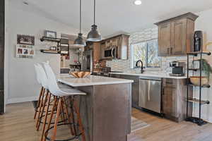 Kitchen featuring light wood finished floors, light countertops, backsplash, appliances with stainless steel finishes, and a kitchen breakfast bar