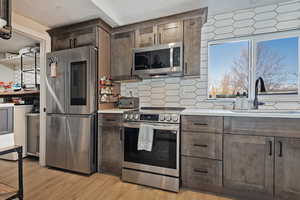 Kitchen with stainless steel appliances, a sink, light countertops, decorative backsplash, and light wood finished floors