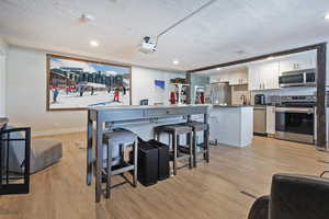 Kitchen with a breakfast bar area, stainless steel appliances, decorative backsplash, white cabinets, and light wood-type flooring