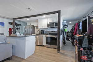 Kitchen with light wood finished floors, tasteful backsplash, white cabinets, appliances with stainless steel finishes, and a textured ceiling