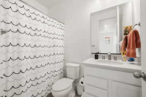 Bathroom with toilet, a shower with shower curtain, and vanity