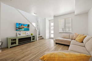 Living area with light wood-style flooring, stairway, visible vents, and baseboards