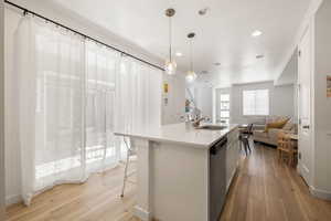 Kitchen featuring light wood finished floors, light countertops, open floor plan, a sink, and dishwasher