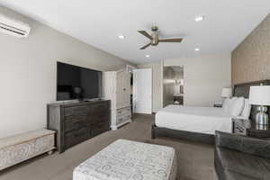 Carpeted bedroom with ensuite bath, a ceiling fan, an AC wall unit, and recessed lighting