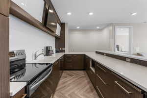 Kitchen with electric range, modern cabinets, light countertops, and dark brown cabinets