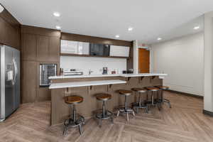 Kitchen with stainless steel refrigerator with ice dispenser, a breakfast bar area, recessed lighting, light countertops, and modern cabinets