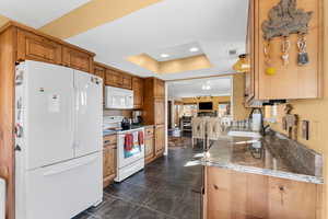 Kitchen with brown cabinets, a raised ceiling, visible vents, a sink, and white appliances