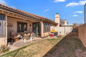 Rear view of house featuring a fenced backyard, a yard, stucco siding, a chimney, and a patio area