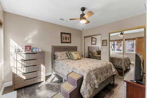 Tiled bedroom with multiple closets, visible vents, ceiling fan, and baseboards