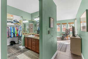 Full bath featuring tile patterned flooring, a walk in closet, vanity, and baseboards