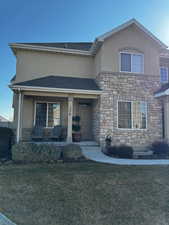 View of front facade featuring a porch, stone siding, roof with shingles, stucco siding, and a front lawn