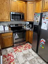 Kitchen with appliances with stainless steel finishes, dark stone counters, brown cabinets, and light tile patterned floors