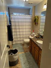 Full bathroom featuring visible vents, a shower with shower curtain, toilet, a textured wall, and vanity