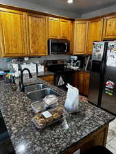 Kitchen featuring appliances with stainless steel finishes, dark stone counters, brown cabinetry, and a sink