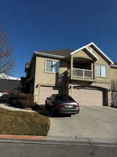 View of front facade with driveway, a balcony, stone siding, an attached garage, and stucco siding