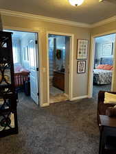 Corridor featuring a textured ceiling, dark colored carpet, ornamental molding, and baseboards