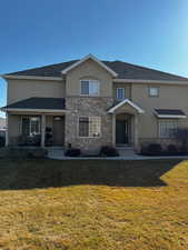 Traditional home featuring stone siding, a front lawn, and stucco siding