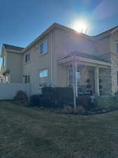 View of side of home with stone siding, a lawn, fence, and stucco siding