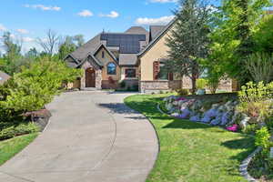 View of front of property featuring roof mounted solar panels, stucco siding, a front yard, and stone siding