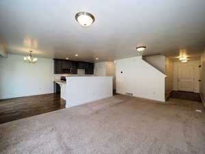 Unfurnished living room with baseboards, visible vents, a textured ceiling, carpet floors, and a chandelier