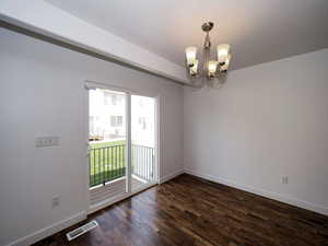 Spare room featuring baseboards, visible vents, a chandelier, and dark wood finished floors