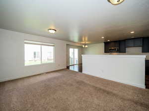 Unfurnished living room featuring dark colored carpet, a notable chandelier, baseboards, and recessed lighting