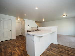 Kitchen featuring dark wood finished floors, a breakfast bar area, light countertops, and a sink