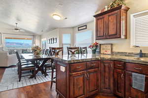 Kitchen with a textured ceiling, lofted ceiling, a peninsula, visible vents, and dark wood-style floors