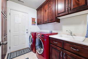 Washroom featuring visible vents, cabinet space, a sink, a textured ceiling, and washer and dryer