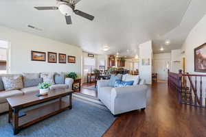 Living room with visible vents, a textured ceiling, baseboards, and wood finished floors