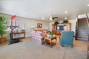 Living room with a textured ceiling, recessed lighting, light colored carpet, a ceiling fan, and stairway