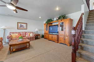 Living room with ceiling fan, recessed lighting, light colored carpet, visible vents, and stairs